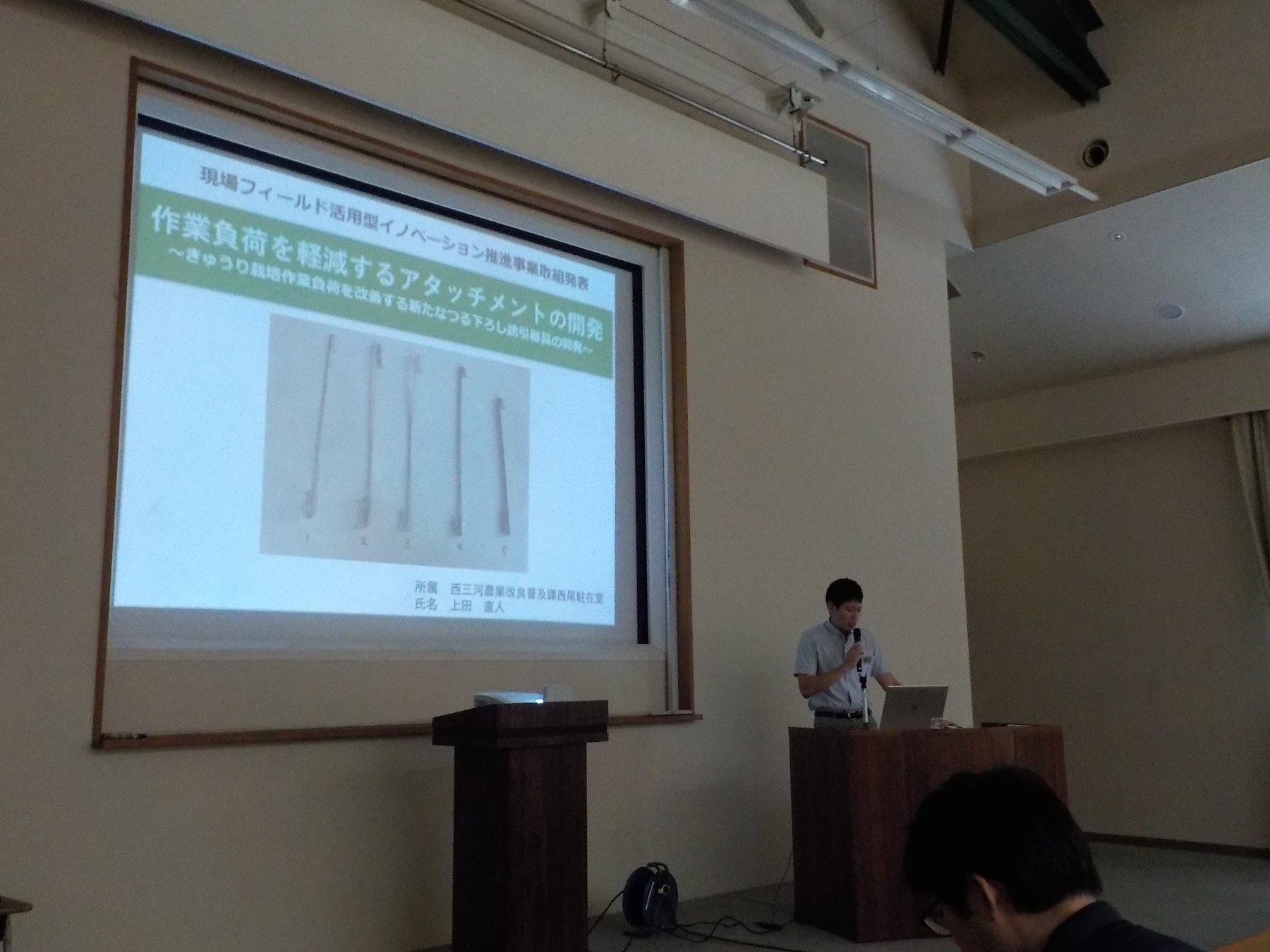 愛知県立農業大学校での講演。スクリーンに試作品が5本並んだスライドが映っている